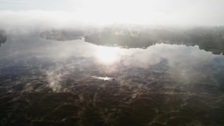 Solo rower training alone at dawn on a serene lake with sunshine and whispy clouds