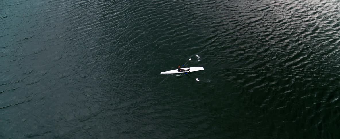 Birds eye view of a man in a white boat against dark water with high contrast