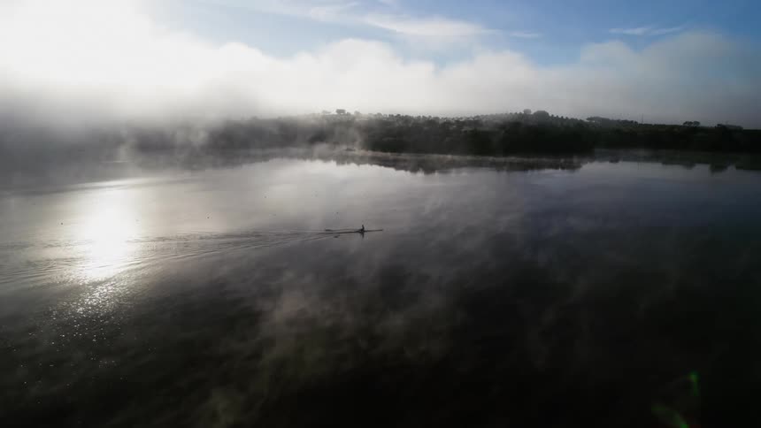 Olympic rower trains in the early morning glow of dawn on flat water with gentle cloud drifts