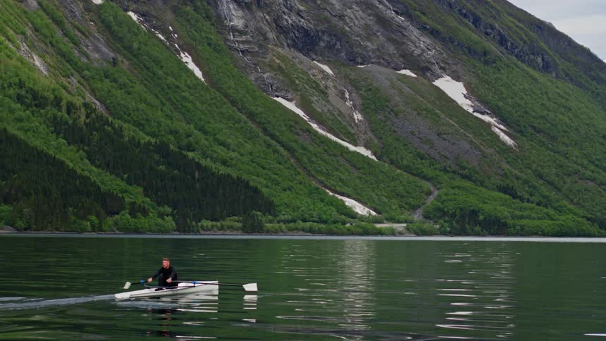 Man canoeing on a lake with mountains around in winter