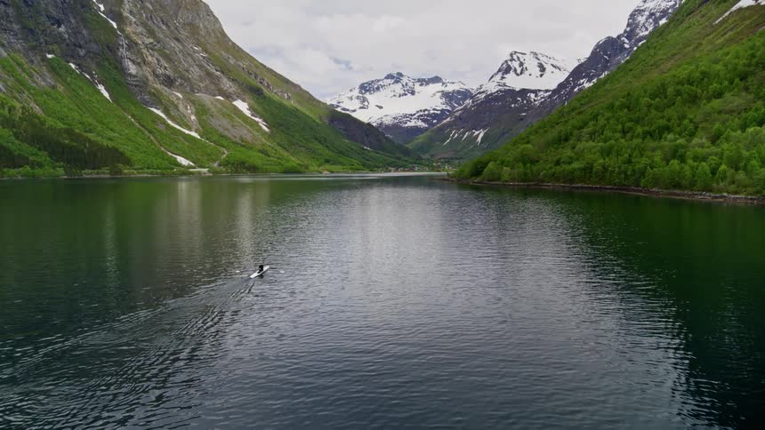 A man rows a boat on serene water in the splendor of the Norwegian fjords