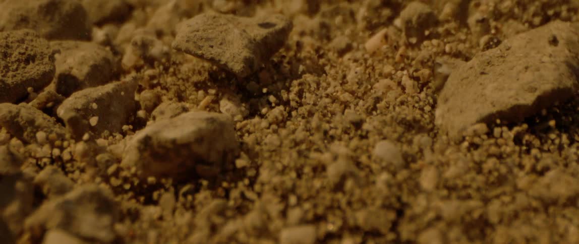 Closeup on the ground with sand and stone rising and falling in slow motion