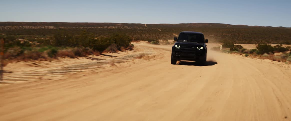Black jeep driving along a desert dirt road on a cloudless blue sky day