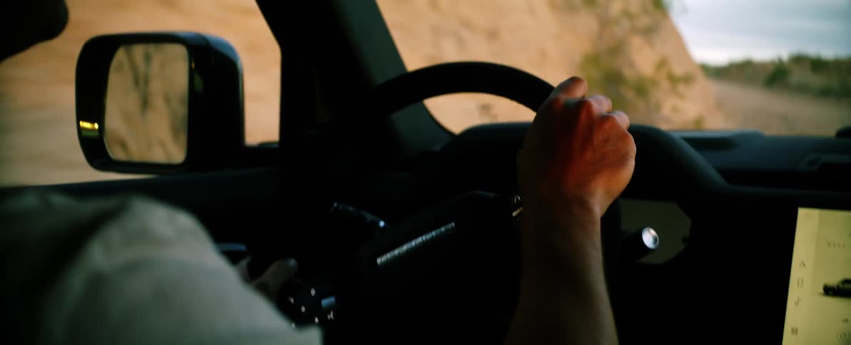 Closeup on the arms of a man driving a vehicle on a dirt road