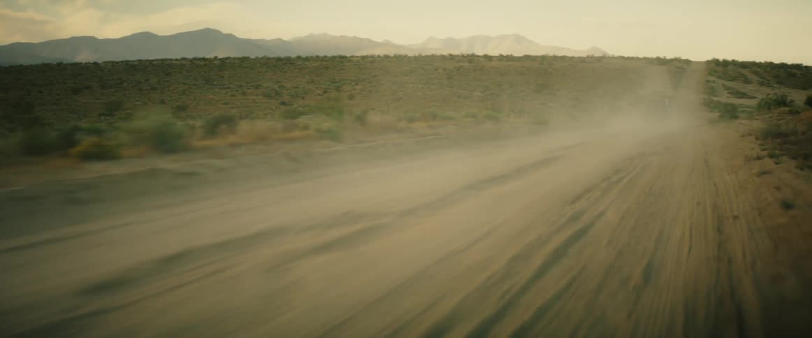 A jeep drives very fast along a dusty road in the desert