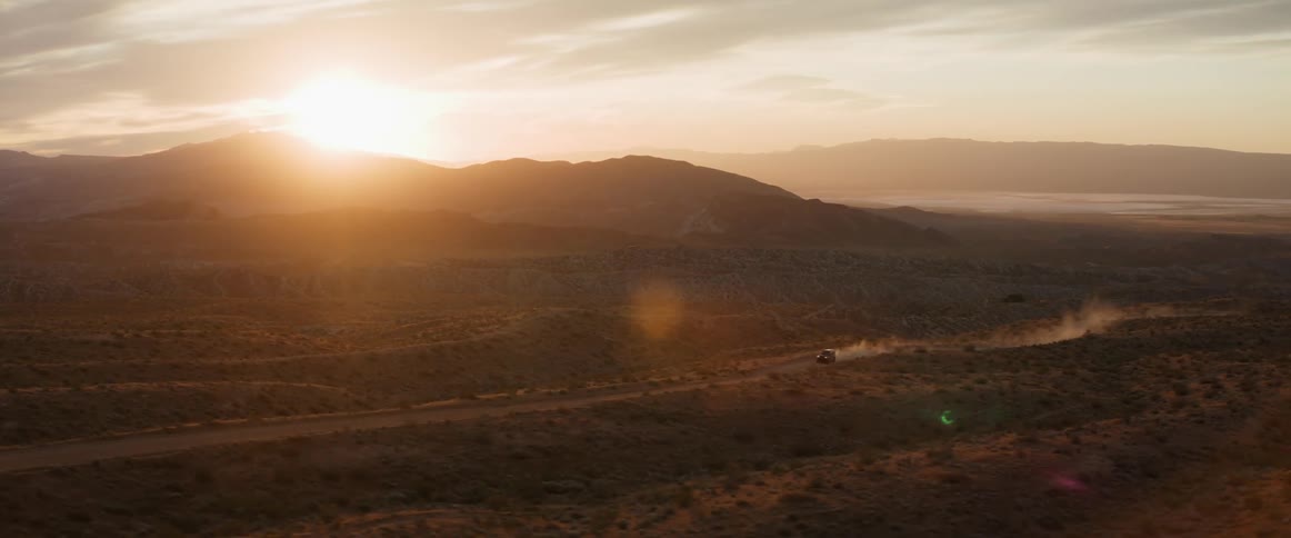 A car driving across the desert as the sun sets behind a hill