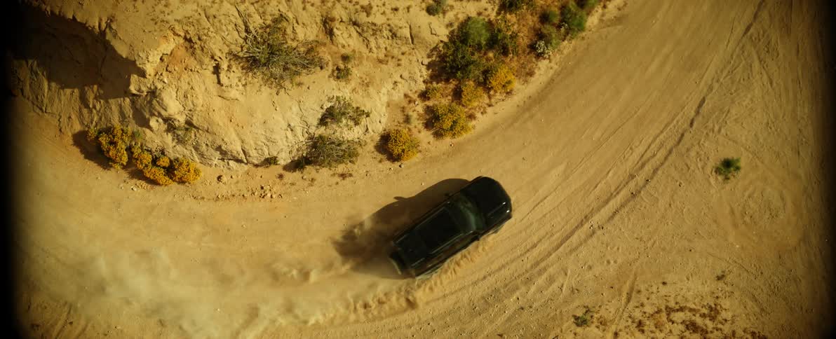 An automobile navigates around a tight corner of a dirt road