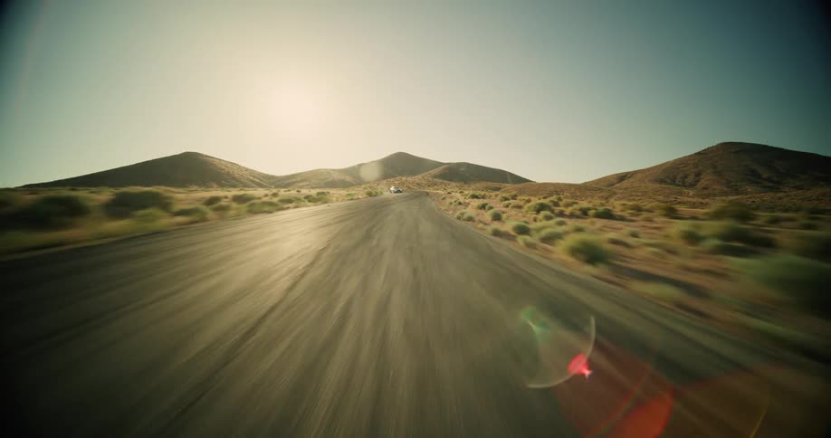 White car speeds down the empty road in the center of the desert