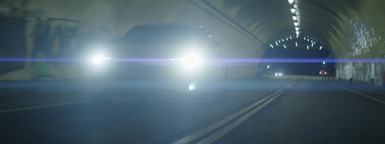 A black sedan car driving out of a tunnel at night