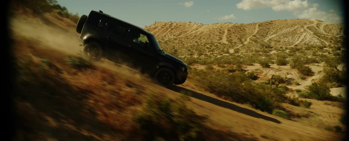 A vehicle drives down a steep road in a desert