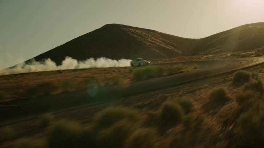 White bmw coup drifting and a road giving off smoke and surrounding mountains