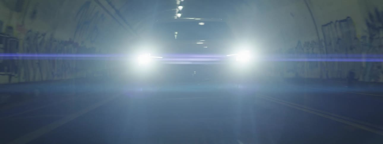 Silver vehicle with front lights on going through a tunnel in the city at night
