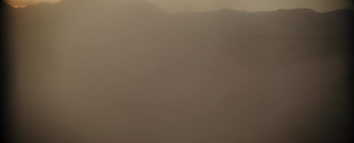 A vehicle is driving on a dirt road kicking up dust in a desolate landscape at dusk