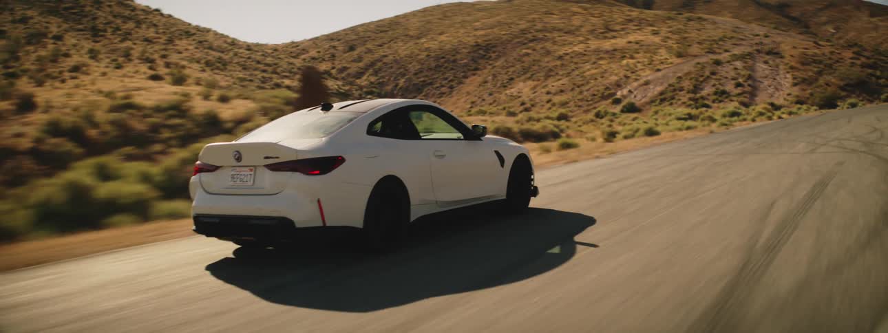 White bmw and sports car traveling along a road next to mountains