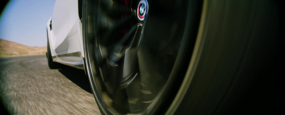 A cars wheel is in motion on a road with a desert landscape in the background