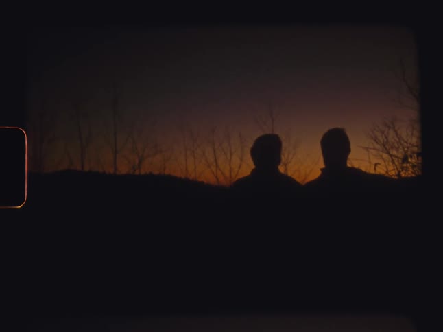 Two people stand outdoors as the sun shines below the horizon