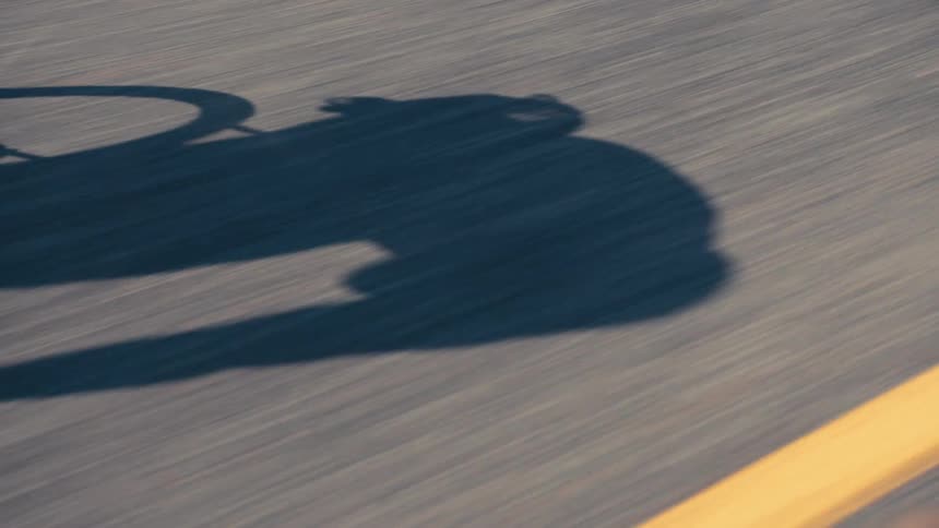 Closeup on the legs and wheels of a person cycling on a road with their shadow on the street