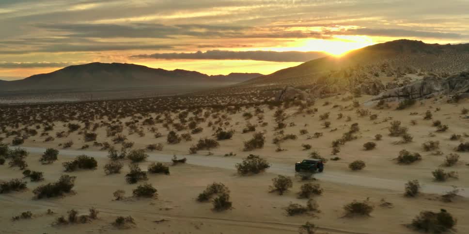 Black jeep is driving on a desert dirt road with a sunset on the horizon