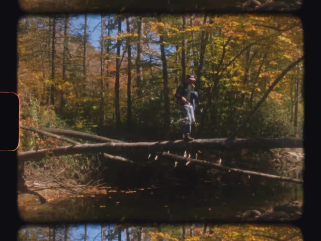 A man walks over a tree suspended over a creek