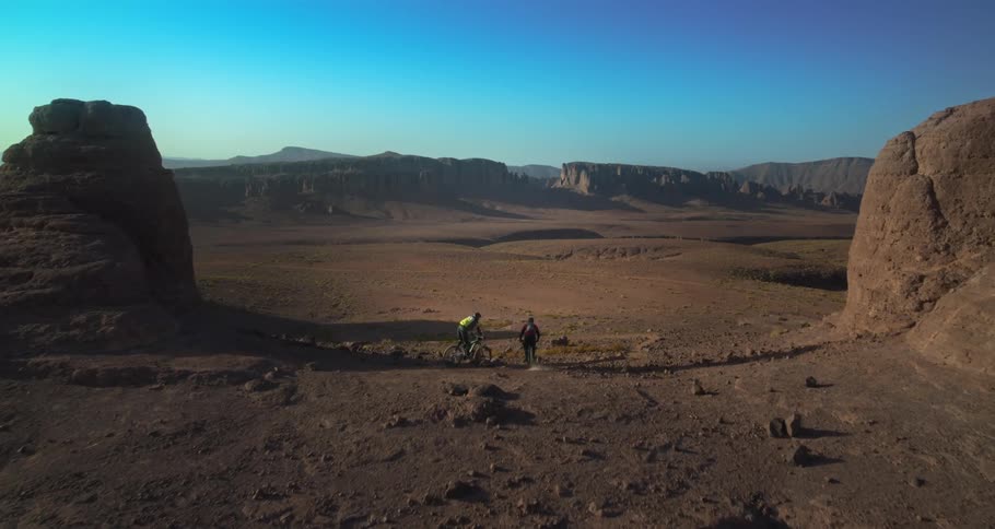Two men cycling in a desert area at midday