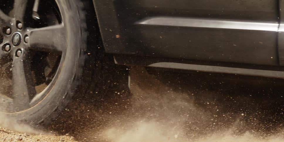A truck driving off road throws sand as it turns
