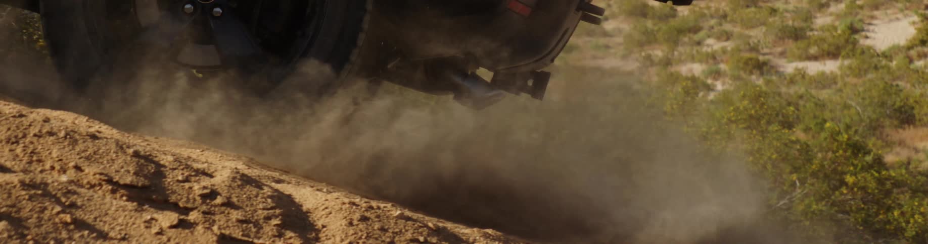 Wheels of a vehicle climbing a sandy slope in a natural environment releasing smoke and dust and a slomojo