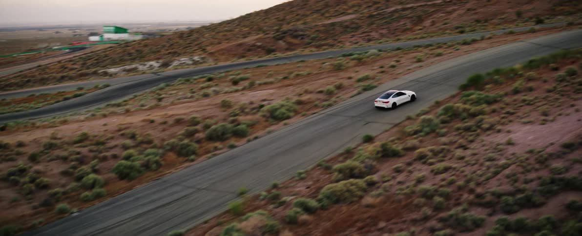 Aerial view of a white car driving on a road on the hills
