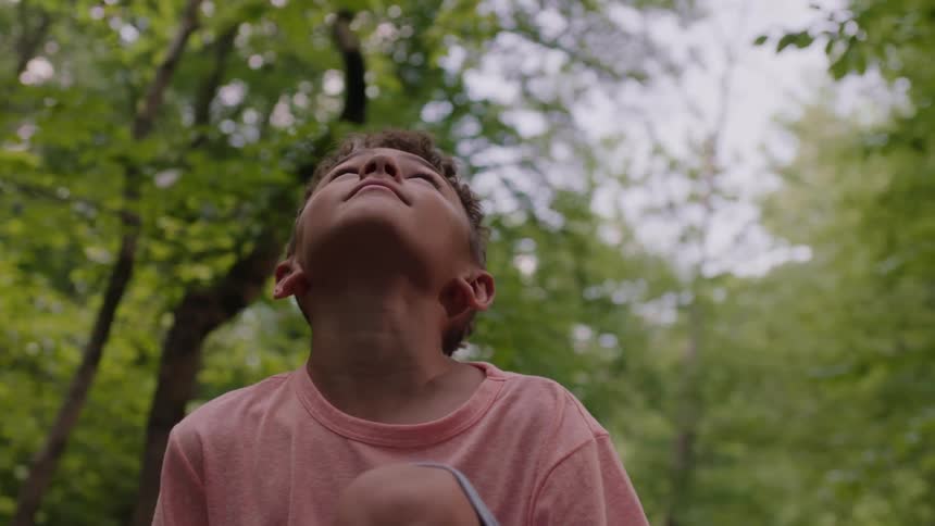 Young boy sitting in a forest looking at the sky