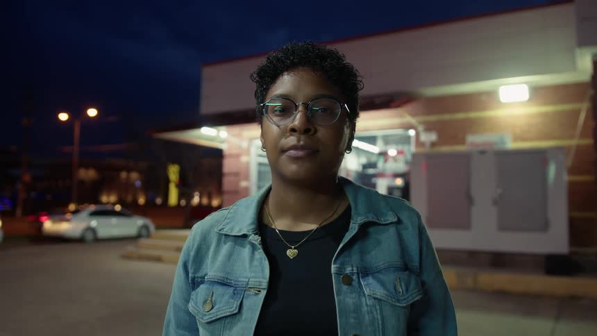 A black woman wearing glasses and standing in the middle of the street