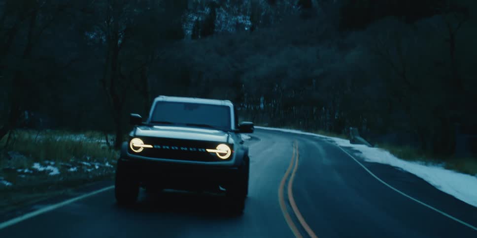 A car on a road between mountains and a snowcovered forest at dusk