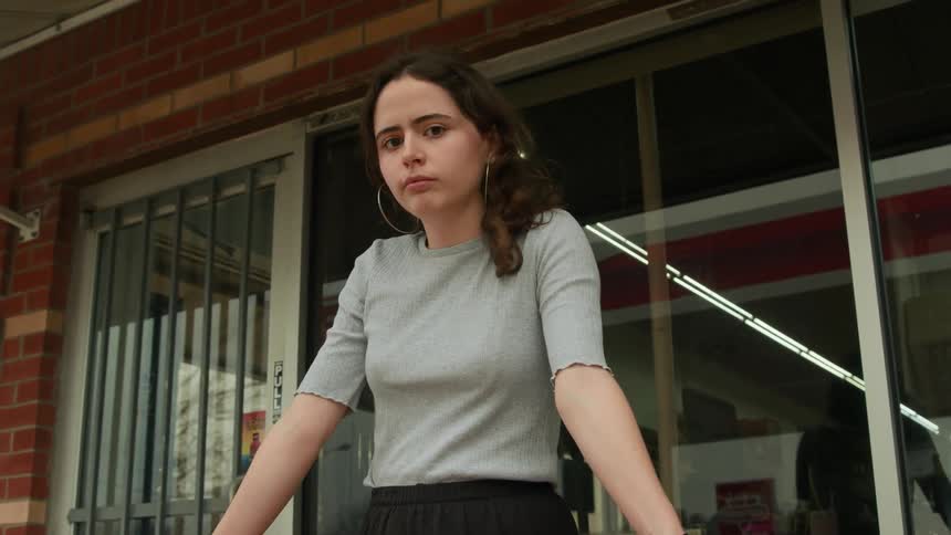 A young woman leaning against a handrail waiting for something with a serious expression