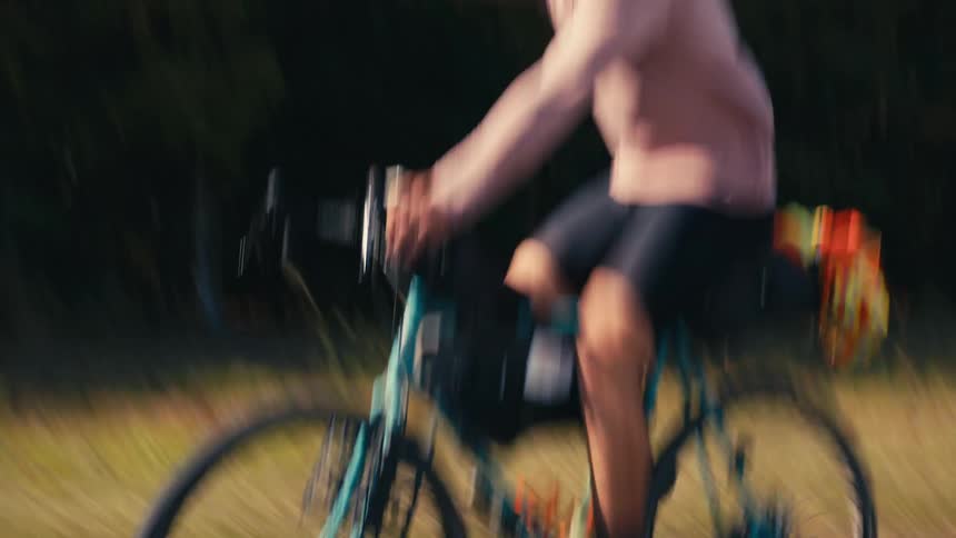 Man cycling along a road next to a forest and drinking water