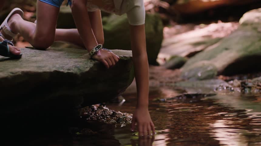 Brother and sister crouch on a rock and pull rocks out of the shallow stream