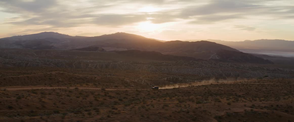 A vehicle travels on a dirt road by the mountains