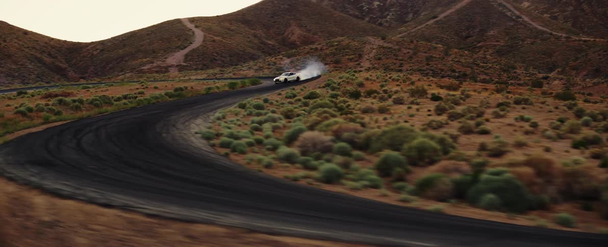 Sporty white bmw turning along a road and releasing tire smoke in a desert location