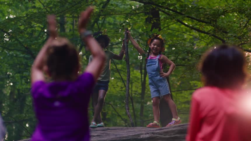 Children are playing over a rock in a forest at sunset