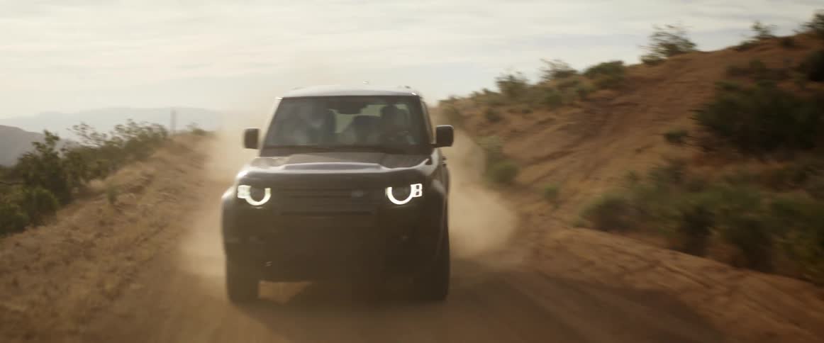 A vehicle is driving kicking dust on a dirt road on arid terrain