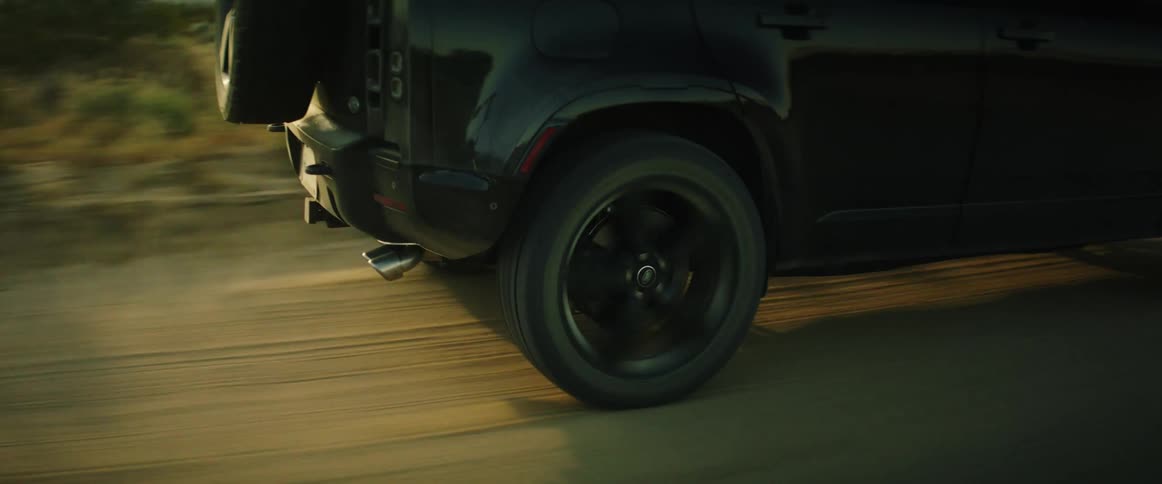 A car is driving on a dirt road kicking up dust
