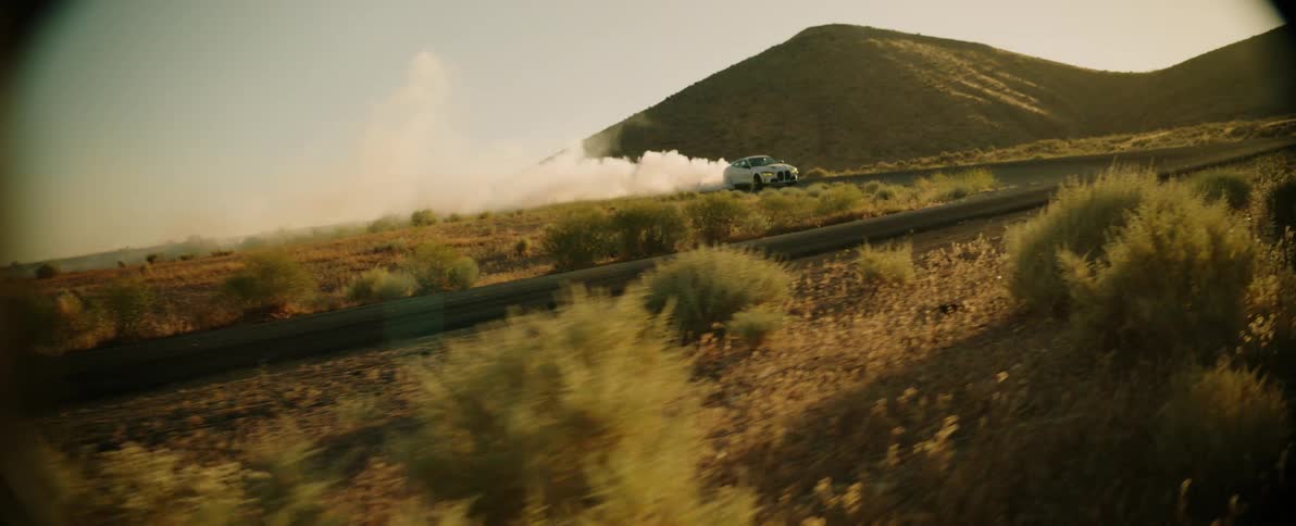 White bmw coup drifting on a smokeemitting road with mountains around