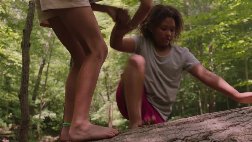 A girl helps another girl climb onto a huge log