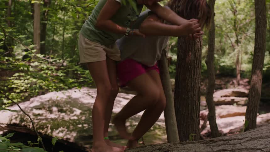 Two little girls climbing a tree trunk lying in the forest