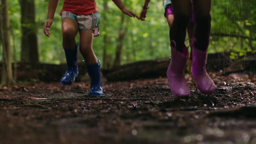 Three children jump around in puddles as it rains