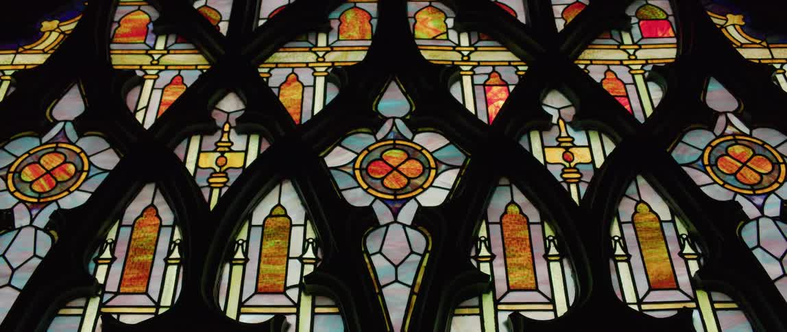 A stained glass window in blue orange and yellow with black wood