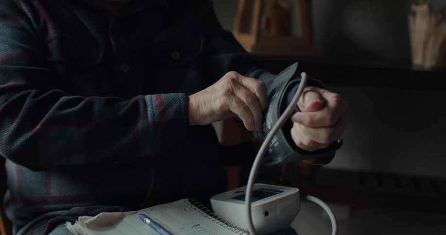 An elderly man puts a blood pressure cuff on his arm