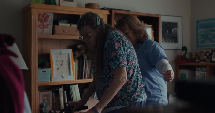 A nurse assisting an elderly woman using a walker at home