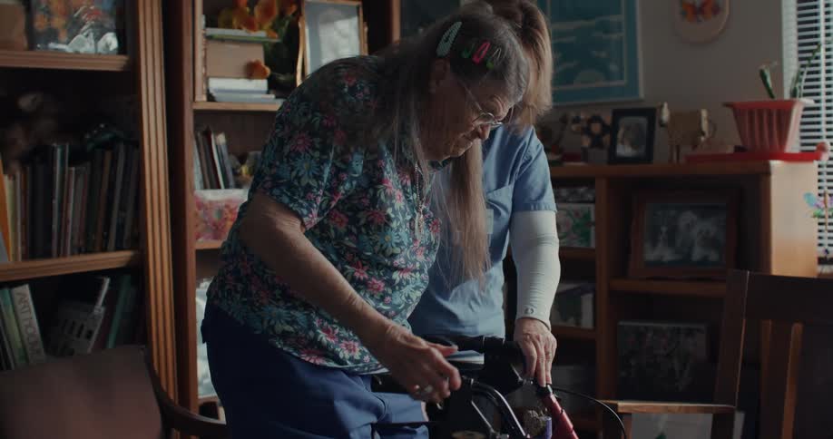 A nurse is assisting another person with a walker in an environment surrounded by various objects