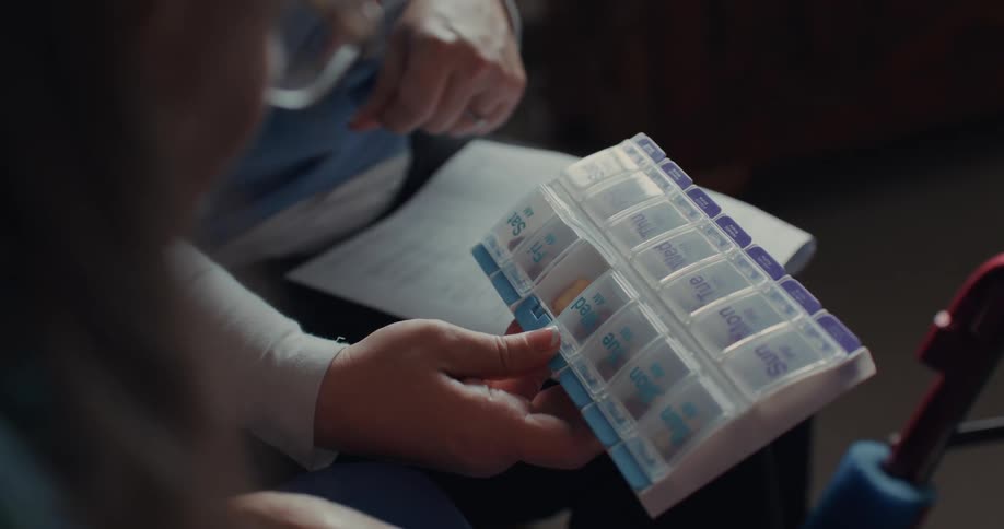 A doctor is holding a container with various medicines and pointing at it while talking to a person who is sitting