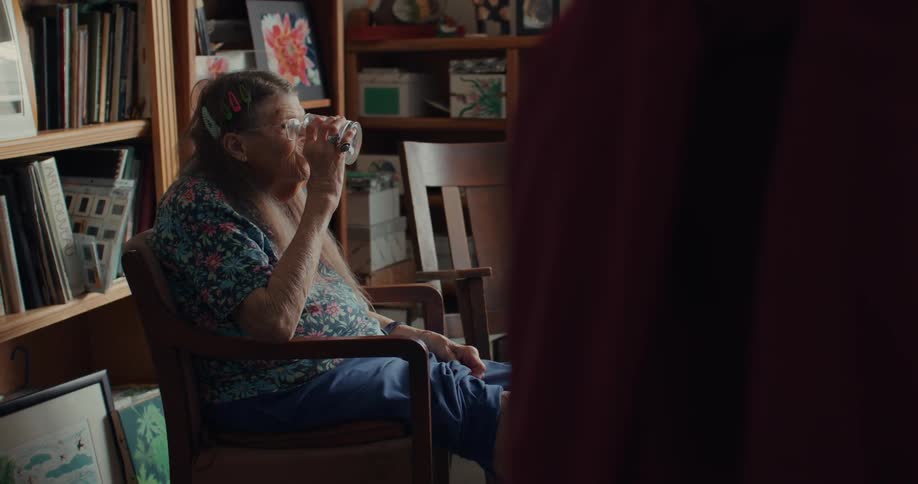 An elderly woman drinks a glass of water