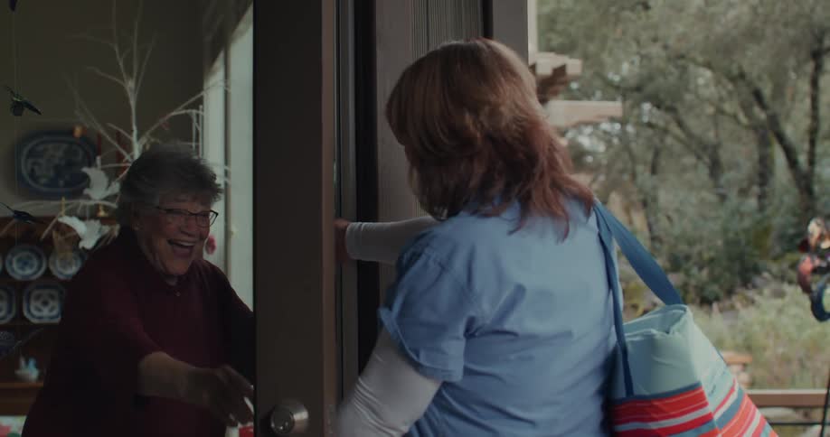 Elderly mother embraces her daughter as she lets her inside the house