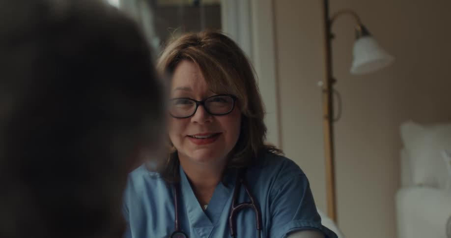 A person dressed in medical attire talks to another person sitting in a bright room